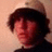 A pixelated image split into two sections: a person with dark hair and a light cap on the left, and red background with black text on the right.