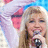 A pixelated image of a person with light brown hair holding a microphone, wearing pink ear-like accessories against a pastel background.