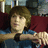 Pixelated image of a person with light brown hair wearing blue clothing and dark wristbands, holding an object against a blurred background.