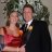 A pixelated static image shows two people in formal attire standing close together against a blurred background.