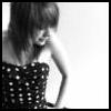 Black-and-white image of a person with short dark hair wearing a polka-dot top, head turned slightly left, hand near shoulder.
