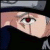 Pixelated close-up of a person's face with light skin tone, dark hair, and a red eye, wearing a dark top against a dark background.
