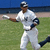 A baseball player in white uniform running on a field with blue background.