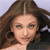 A pixelated close-up of a person with long brown hair parted in the middle, wearing a dark top against a light background.