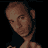 Pixelated static image of a person's head and shoulders with brown hair, visible facial features including eyes and nose, and dark clothing against a black background.