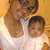 A woman in a white top holds a baby against a light brown background; the image shows slight pixelation and color variation across frames.