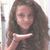 A pixelated image of a person with long brown hair holding a white rectangular object near their chest against a light background.