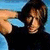 Pixelated image of a person with dark hair in a black top, hand raised near head, next to black background with white text and arrow symbol.