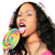 A person with long dark hair sings into a colorful spiral-patterned microphone, wearing a pink top against a white background.
