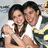 Two people embrace in a close-up pose with one person's arm around the other, both smiling against a blurred background.