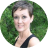 Circular pixelated image of a person with short dark hair wearing a black sleeveless top against green foliage background.