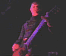 A musician plays a red electric guitar under stage lights, with light flares shifting across the scene.