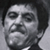 Static grayscale pixelated image of a human face with dark hair and formal attire, likely from a film still or character portrait.