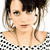 Pixelated close-up of a person with dark hair and light skin wearing large hoop earrings, a black-and-white checkered top, and visible necklaces.