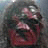 Pixelated static image of a figure with dark hair and red clothing against a muted background, showing no visible text or distinct symbols.