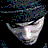 Pixelated static icon of a stylized face with abstract background elements, featuring gray and white tones with pink highlights against dark blue and teal pixel clusters.