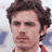 Static 48x48 pixel buddy icon showing a close-up of a person's face with dark curly hair, red clothing collar, and blurred background elements.