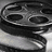 Black-and-white film reel with visible sprocket holes and partial film strip, positioned above a stylized chair base with four curved legs.