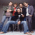 Group of people posing together with one person holding a camera, red text 'FAN' on white background.