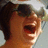 Pixelated image of a person with short brown hair wearing dark sunglasses and a light-colored cap, mouth open in an exaggerated expression.