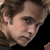 Pixelated close-up of a person's face with light brown hair, visible ear, and neutral expression against a dark background.