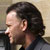 Pixelated profile view of a person with dark hair holding a microphone against a light background.
