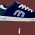 Animated sequence of dark blue sneakers with light blue 'M' logo on side, white laces, and gray soles against brown background; text changes from "i hate preps" to "in skater shoes".
