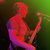Pixelated figure in red and purple hues holding a long object against a dark green gradient background.