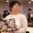 Pixelated image of a person in a white shirt with a colorful graphic, standing among other people in a blurred indoor setting.