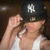 A person wearing a black baseball cap with white NY logo adjusts the cap while standing against a dark background.