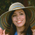 A pixelated close-up of a person wearing a light-colored wide-brimmed hat and a blue top, with long dark hair and a smiling expression.