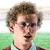 Pixelated image of a person with curly brown hair and glasses against green background, next to golden-brown fried food in white bowl.