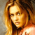 Pixelated portrait of a person with long light brown hair, wearing a dark top, against a muted background with warm tones.