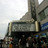 Pixelated static image showing a building facade with a prominent vertical structure and horizontal banding under a light sky.