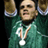 Pixelated static image of a person in green sports attire holding two trophies with medals around their neck.