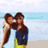 Two pixelated figures embrace on a beach with light blue water and sky background.
