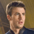 Pixelated close-up of a person with short dark hair wearing a dark blue collared shirt against a blurred brown and yellow background.
