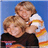 Two people embrace against a blue background; one wears dark clothing, the other white with orange stripes.