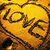 A pixelated yellow circular icon with dark brown text reading 'LOVE' and a stylized heart symbol, surrounded by decorative swirls.