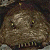 A pixelated static image of a textured, rounded object with a mottled brown and gray surface, featuring small yellow and dark spots, set against a dark background.