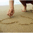 A static image shows a person's hand drawing on sand with bare feet visible, alongside text elements in pixelated font.