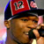 Pixelated close-up of a person wearing a red and black cap with white text, holding a microphone near their mouth.