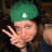 A pixelated image shows a person wearing a green beret with a white cross symbol, making a peace sign with their right hand against a dark background.