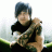 Pixelated static image of a person with dark hair wearing black clothing, holding an object against a blurred background.