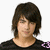 Pixelated static image of a person with short dark brown hair, light skin, and a black top with a purple pattern on the right shoulder.