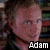 Pixelated close-up of a person's face with light skin tone, visible eyes and nose, and dark hair against a blurred background; white text 'Adam' appears at bottom right.