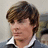 Pixelated close-up of a person with brown hair wearing a white-collared shirt and dark jacket against a light background.