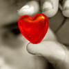 A red heart-shaped object held between fingers in a grayscale background.