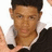 A pixelated close-up of a person with short dark hair wearing a black jacket over a white collared shirt, holding an object near their chest.