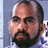 Pixelated close-up of a person's face with light skin, dark eyebrows, and a dark beard, set against a blue and white background.